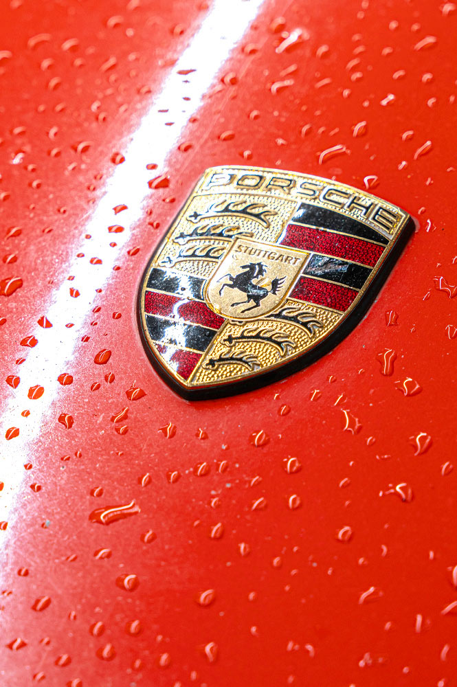 Porsche Emblem auf rotem Lack mit Regentropfen